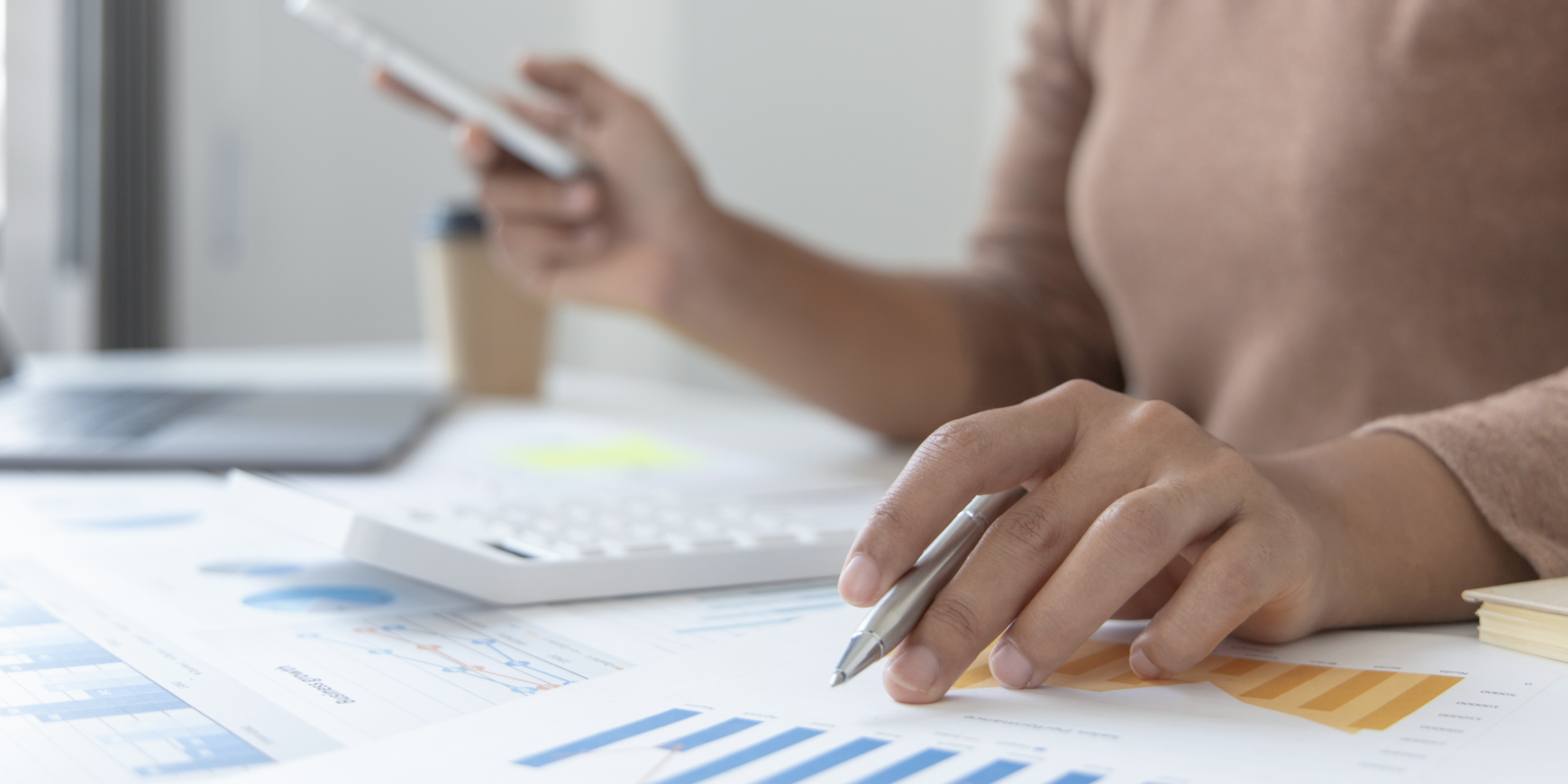 A close-up image of a person's hand holding a pen, hovering over a document on a table.